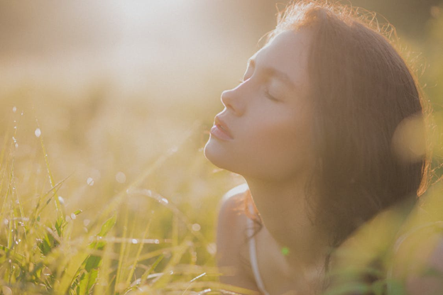 A person with her eyes closed in a field of grass